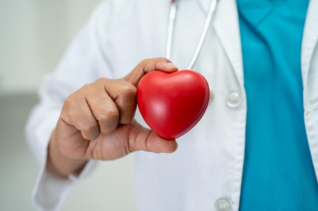 Arzt, der ein rotes Herz in der Krankenstation hält, gesundes, starkes medizinisches Konzept