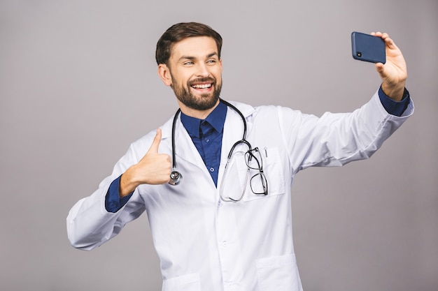 Arzt, der ein Selfie mit Frontkamera nimmt und an seinem Arbeitsplatz lächelt