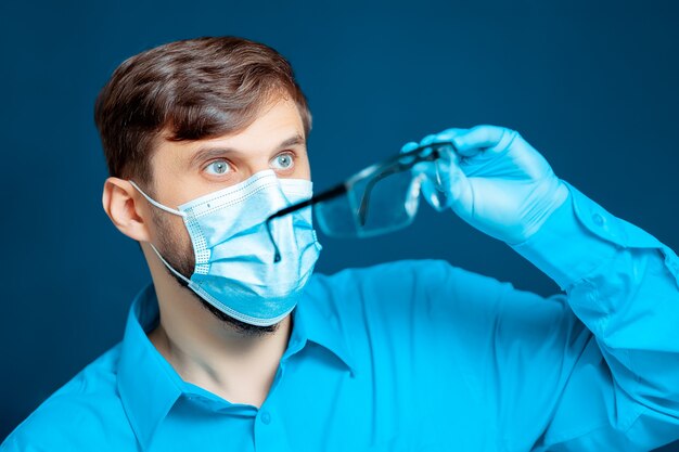 Arzt, der eine Schutzmaske und Handschuhe trägt, setzt eine medizinische Brille auf.