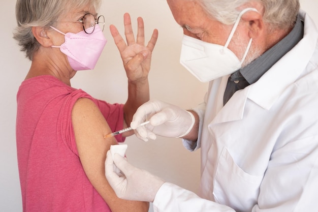 Arzt, der einer älteren kaukasischen Frau eine Injektion gibt, die eine vierte Auffrischimpfung mit Covid-19-Impfstoff erhält, die eine Maske trägt
