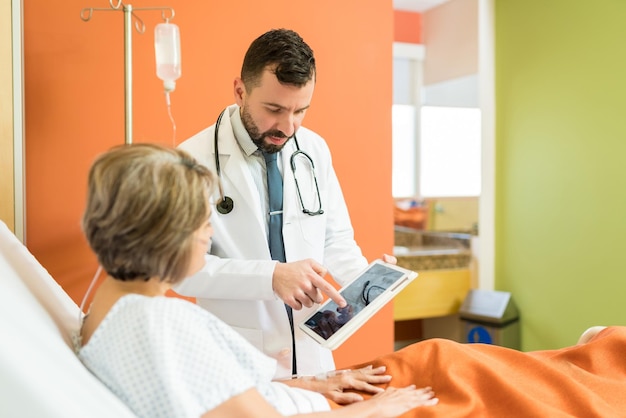 Arzt erklärt älteren patienten im krankenhaus röntgenbilder auf digitalem tablet