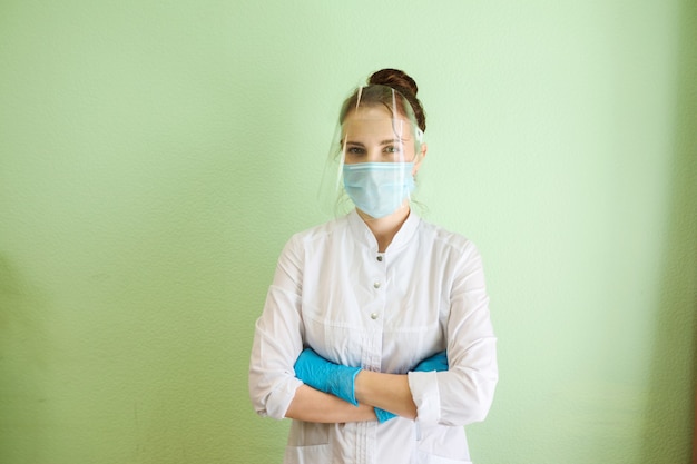 Arzt, Facharzt, Kosmetikerin, Zahnarzt trägt Schutzschild, Maske und Gummihandschuhe. Medizinische Uniform. Grüner Wandhintergrund. Drinnen in der Klinik.