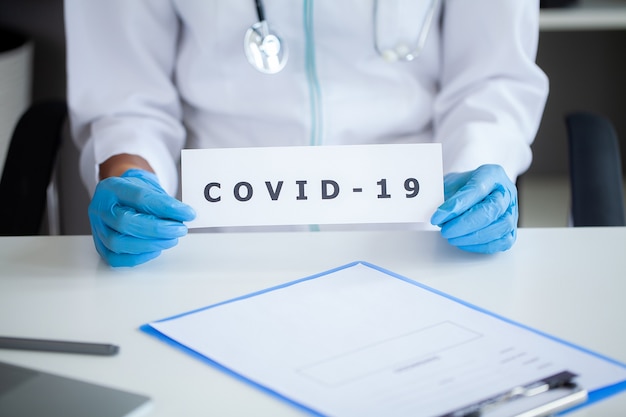 Arzt hält eine Papierkarte mit Text covid-19.