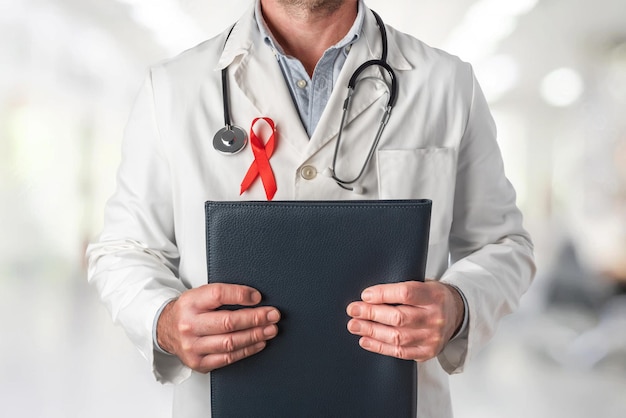 Arzt hält einen Ordner mit medizinischen Berichten und trägt eine rote Schleife auf der Brust Welt-Aids-Tag