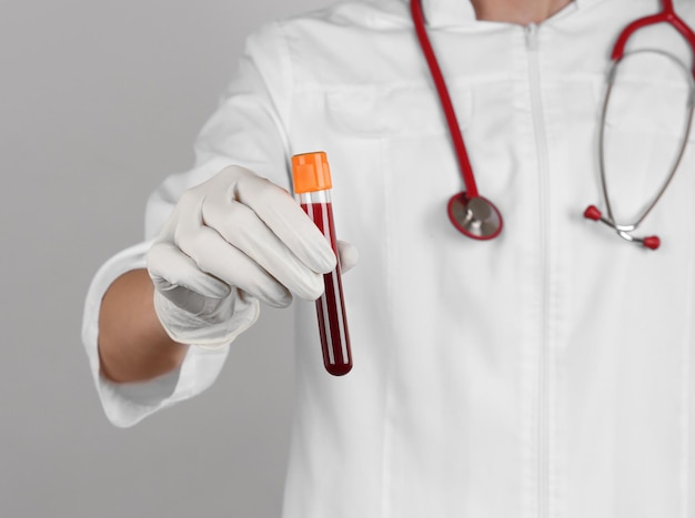 Arzt hält rotes Blut im Reagenzglas auf grauem Hintergrund hautnah