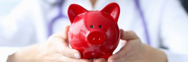 Arzt hält Sparschwein in seinen Händen Krankenversicherungs- und Zahlungskonzept