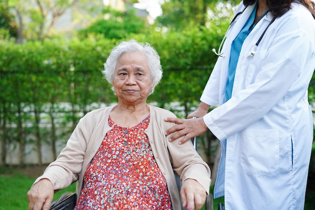 Arzt hilft Behindertenpatientin einer asiatischen älteren Frau, die im medizinischen Konzept des Parks im Rollstuhl sitzt