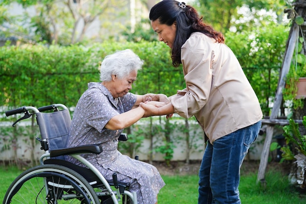 Arzt hilft Behindertenpatientin einer asiatischen älteren Frau, die im medizinischen Konzept des Parks im Rollstuhl sitzt