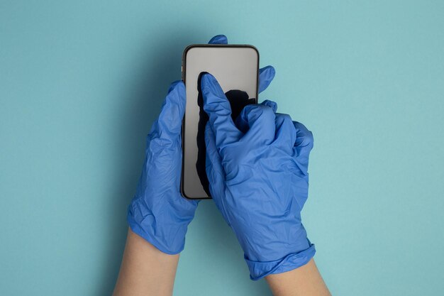 Arzt im blauen Handschuh hält Touchscreen-Smartphone in seinen Händen isoliert auf blauem Hintergrund