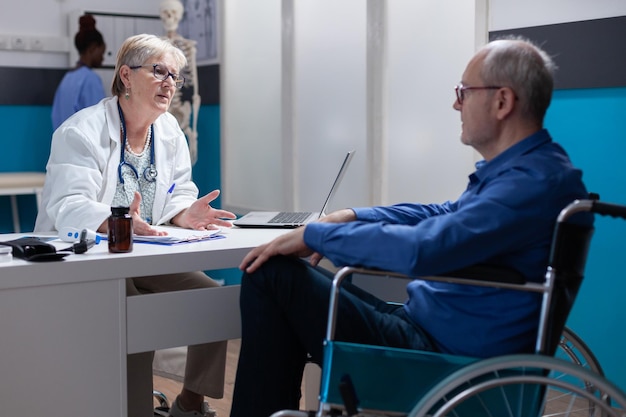 Arzt im Gespräch mit Menschen mit Behinderungen bei der jährlichen Untersuchung im medizinischen Kabinett. Mediziner diskutiert über Gesundheitsversorgung und Behandlung mit Patienten im Rollstuhl. Gesundheitsberatung