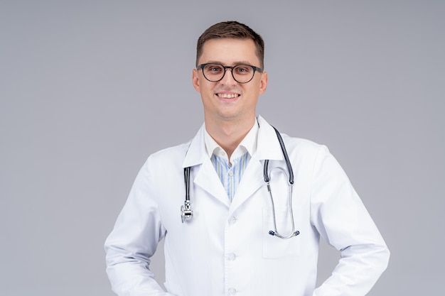 Arzt im weißen Kittel und Phonendoskop am Hals lächelt fröhlich. Sanitäter in blauen Gummihandschuhen. Fotoshooting im Studio.