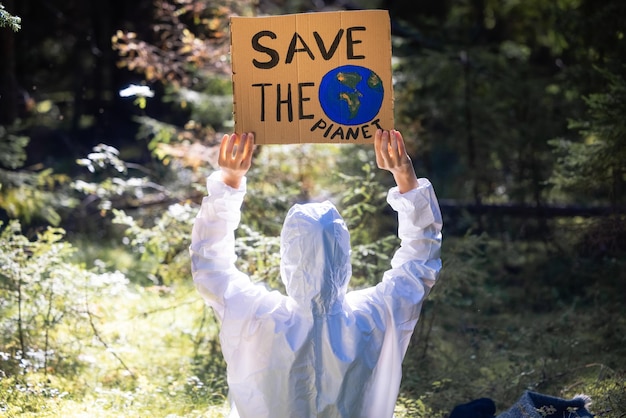 Arzt in einem weißen Anti-Epidemie-Anzug, der ein Pappbanner in den Händen hält. Im Wald.