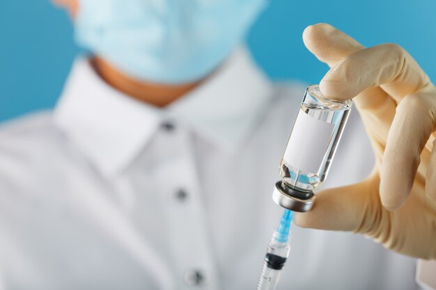 Arzt in Gummihandschuhen hält eine Ampulle mit einem Impfstoff und einer Spritze