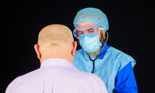 Arzt in Maske mit Stethoskop-Kontrollpatient. Kranker Mann im Krankenhaus. Coronavirus. Gesundheitspflege.