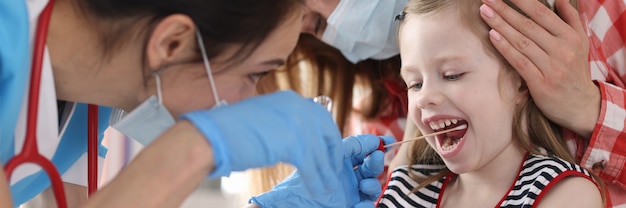 Arzt in medizinischer Schutzmaske, der Wangenabstrich von kleinem Mädchen mit Wattestäbchen nimmt