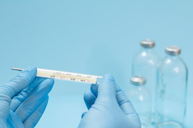 Arzt in Nitrilhandschuhen mit einem Quecksilberthermometer aus Glas auf blauem Hintergrund