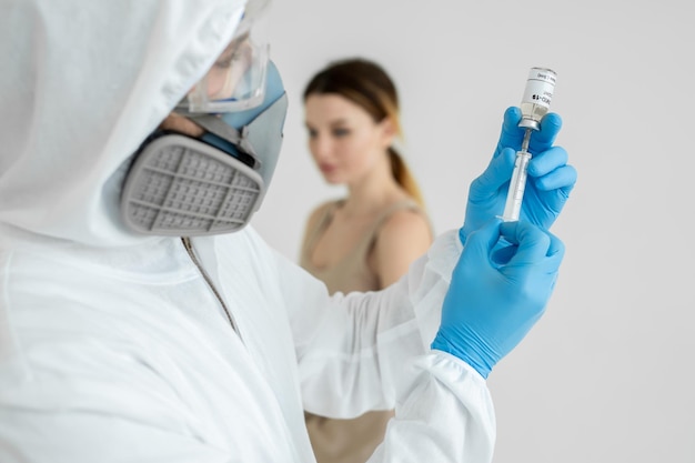 Arzt in Schutzanzug und Maske hält Injektionsspritze und Impfstoff COVID19