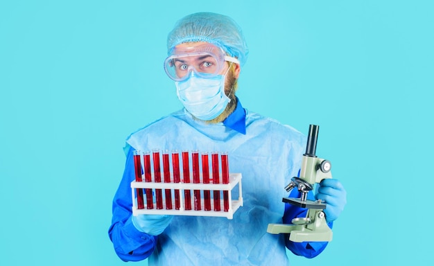 Arzt in Schutzbrille und Maske mit Blutprobenröhrchen und Mikroskop im Labor