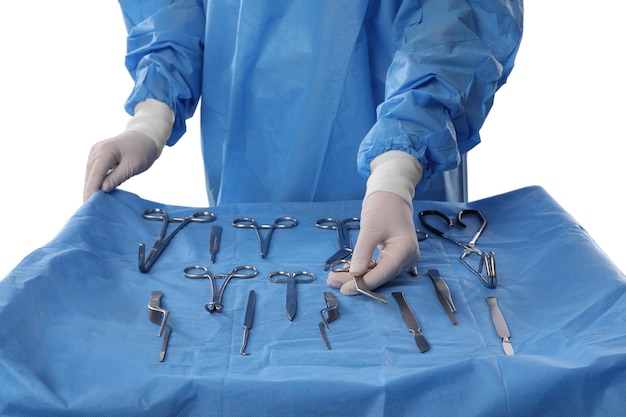 Arzt mit Pott39s-Schere in der Nähe des Tisches mit verschiedenen chirurgischen Instrumenten auf hellem Hintergrund, Nahaufnahme