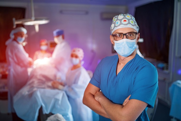 Arzt steht mit gekreuzten Händen in medizinischer Maske Medizinisches Team im Hintergrund Arzt in Brille mit medizinischer Maske im Gesicht Nahaufnahme