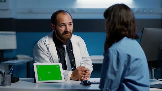 Arzt und Krankenschwester, die über Stunden im Krankenhausbüro arbeiten und die Symptome von Patienten besprechen, die eine Gesundheitsbehandlung planen, um Krankheiten zu heilen. Tablet-Computer mit Green-Screen-Display-Chroma-Key auf dem Tisch