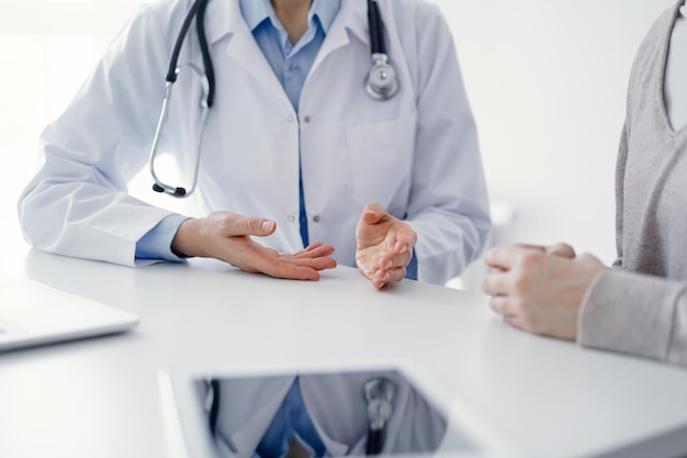 Arzt und Patient besprechen aktuelle Gesundheitsfragen, während sie im Klinikbüro am Tisch sitzen, nur die Hände in Nahaufnahme. Medizinkonzept.