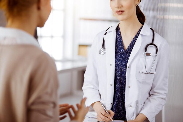 Arzt und Patient besprechen die aktuelle Gesundheitsuntersuchung, während sie in einer sonnigen Klinik sitzen. Perfekte medizinische Versorgung im Krankenhaus.