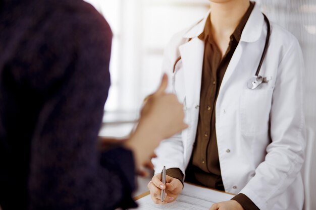 Arzt und Patient besprechen die aktuelle Gesundheitsuntersuchung, während sie in einer sonnigen Klinik sitzen. Perfekte medizinische Versorgung im Krankenhaus.