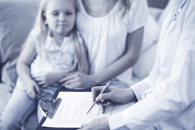 Arzt und Patient. Kinderarzt mit Klemmbrett bei der Untersuchung des kleinen Mädchens mit ihrer Mutter zu Hause. Krankes und unglückliches Kind bei der ärztlichen Untersuchung. Medizin-Konzept.