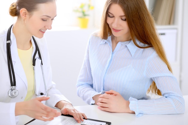 Arzt und Patient sitzen am Schreibtisch am Fenster, Sonne scheint