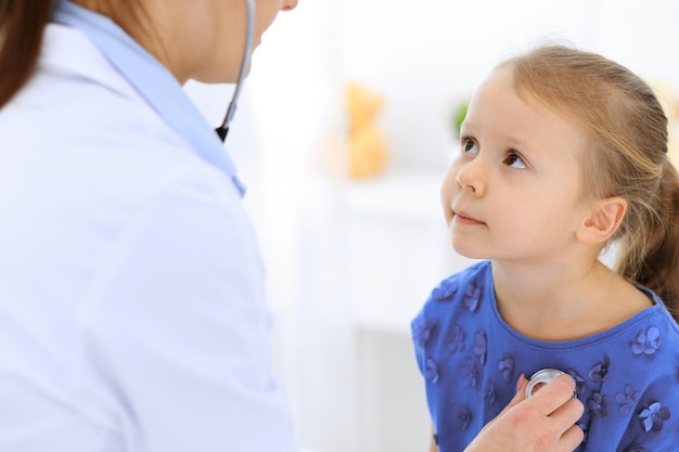 Arzt untersucht ein kleines Mädchen mit einem Stethoskop. Glücklich lächelnder Kinderpatient bei der üblichen ärztlichen Untersuchung. Medizin- und Gesundheitskonzepte.