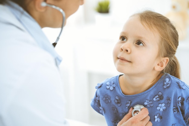 Arzt untersucht ein kleines Mädchen mit einem Stethoskop. Glücklich lächelnder Kinderpatient bei der üblichen ärztlichen Untersuchung. Medizin- und Gesundheitskonzepte.