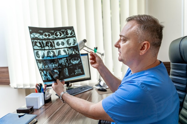 Arzt untersucht Röntgenbild eines Patienten. Männlicher Radiologe, der am Tisch sitzt. Hintergrund der medizinischen Praxis.