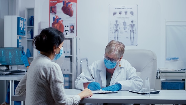 Arztkonsultation während der COVID 19-Gesundheitskrise, Arzt und Patient tragen Masken und sprechen durch eine Plexiglaswand. Medizinische Beratung in Schutzausrüstungskonzeptaufnahme von sars-cov-2 global