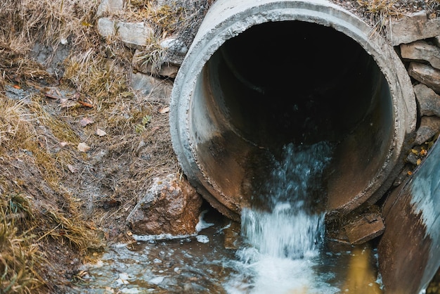 As águas residuais fluem de um cano para o rio Lidar com a poluição Gerenciamento das águas residuais e da ecologia dos rios Águas tóxicas com mau cheiro