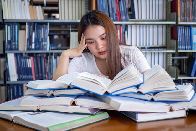 As alunas ficam estressadas ao ler muitos livros colocados nas mesas da biblioteca. para se preparar para o exame