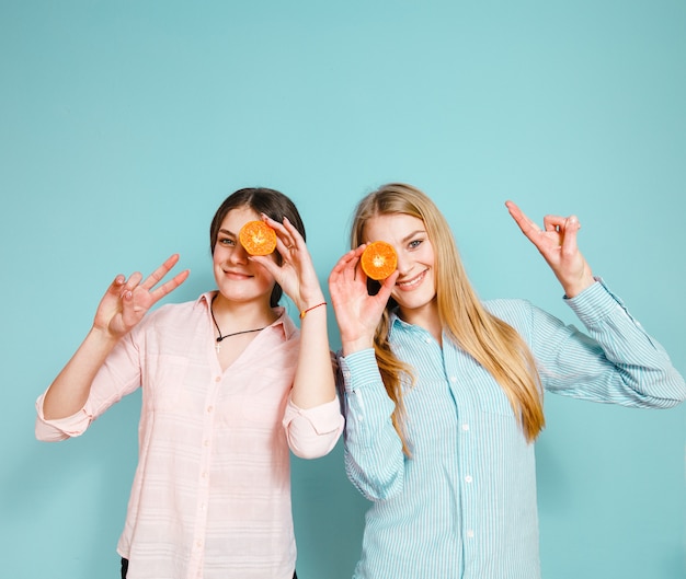 As amigas felizes riem e escondem seus olhos com fatias de mandarim sobre o fundo azul