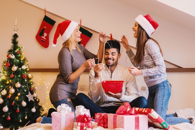 As amigas que colocam luzes de Natal nos amigos se divertem enquanto ele come pipocas.