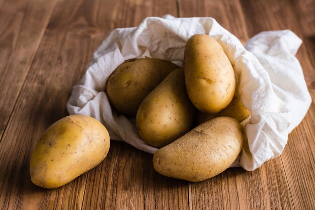 As batatas são derramadas do saco em uma mesa de madeira