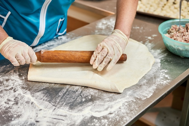 As chefes femininas estendem a massa com rolo para cozinhar bolinhos, ravióli ou khinkali