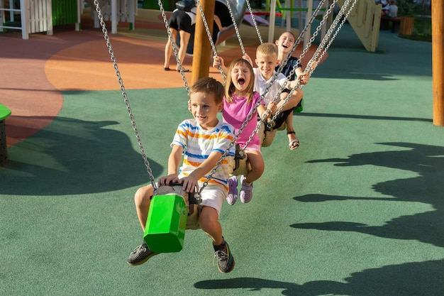 As crianças andam em um longo balanço em um playground moderno, sentam-se umas atrás das outras e riem