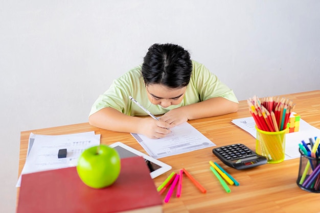 As crianças asiáticas estão estudando exercícios com determinação na mesa de estudo há artigos de papelaria de equipamentos de estudo