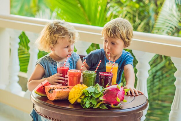 As crianças bebem vitaminas saudáveis e coloridas. melancia, mamão, manga, espinafre e fruta do dragão. smoothies, sucos, bebidas, variedade de bebidas com frutas frescas em uma mesa de madeira