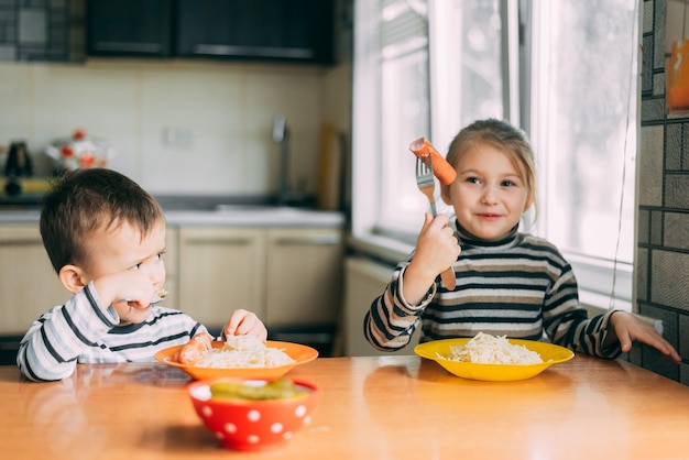 As crianças comem massa e salsicha na cozinha