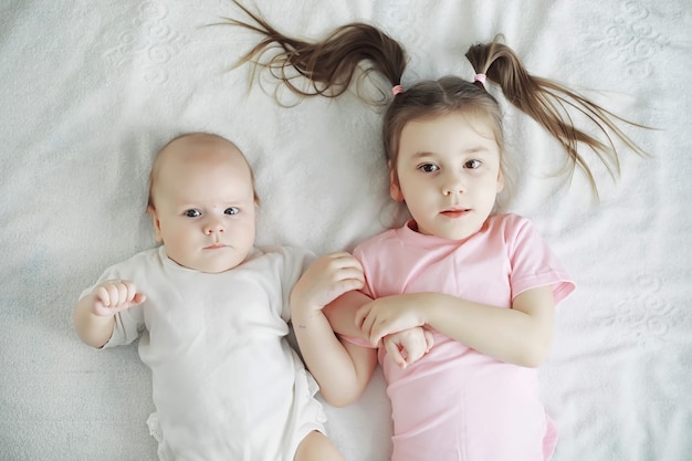 As crianças deitam-se na cama ao lado do bebê recém-nascido, a irmãzinha. emoções infantis.