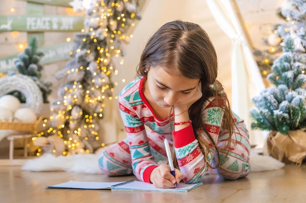 As crianças escrevem uma carta para o Papai Noel debaixo da árvore Foco seletivo