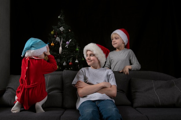 As crianças estão à espera de presentes de Natal. Três crianças com chapéus de Papai Noel.