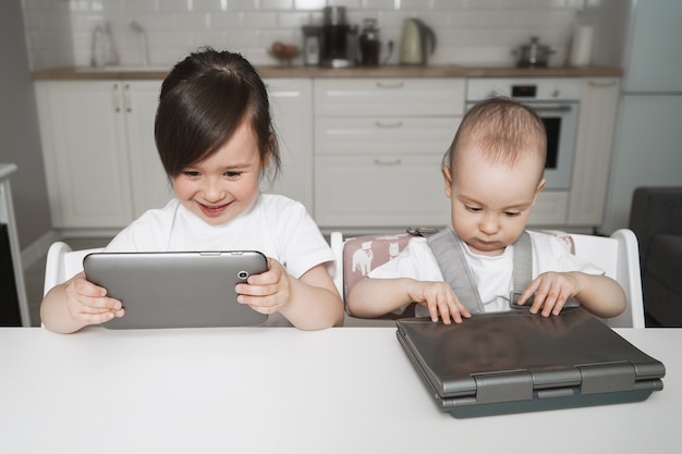 As crianças estão sentadas com aparelhos. Educação a distância para crianças. Menina sentada com um tablet e laptop. Infância digital moderna. Crianças assistem muito a desenhos animados