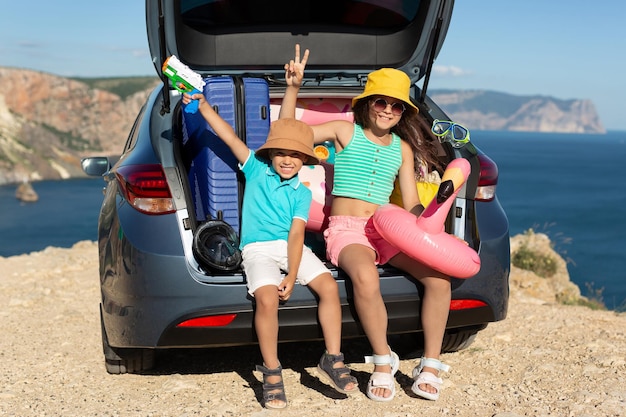 As crianças estão sentadas no porta-malas de um carro com círculos infláveis de malas perto do mar