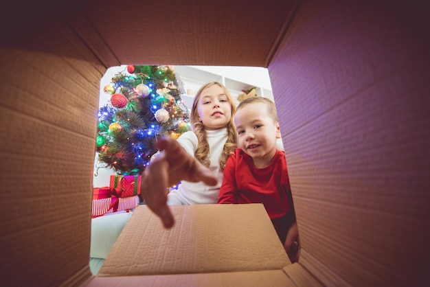 As crianças felizes abrem a caixa perto da árvore de natal